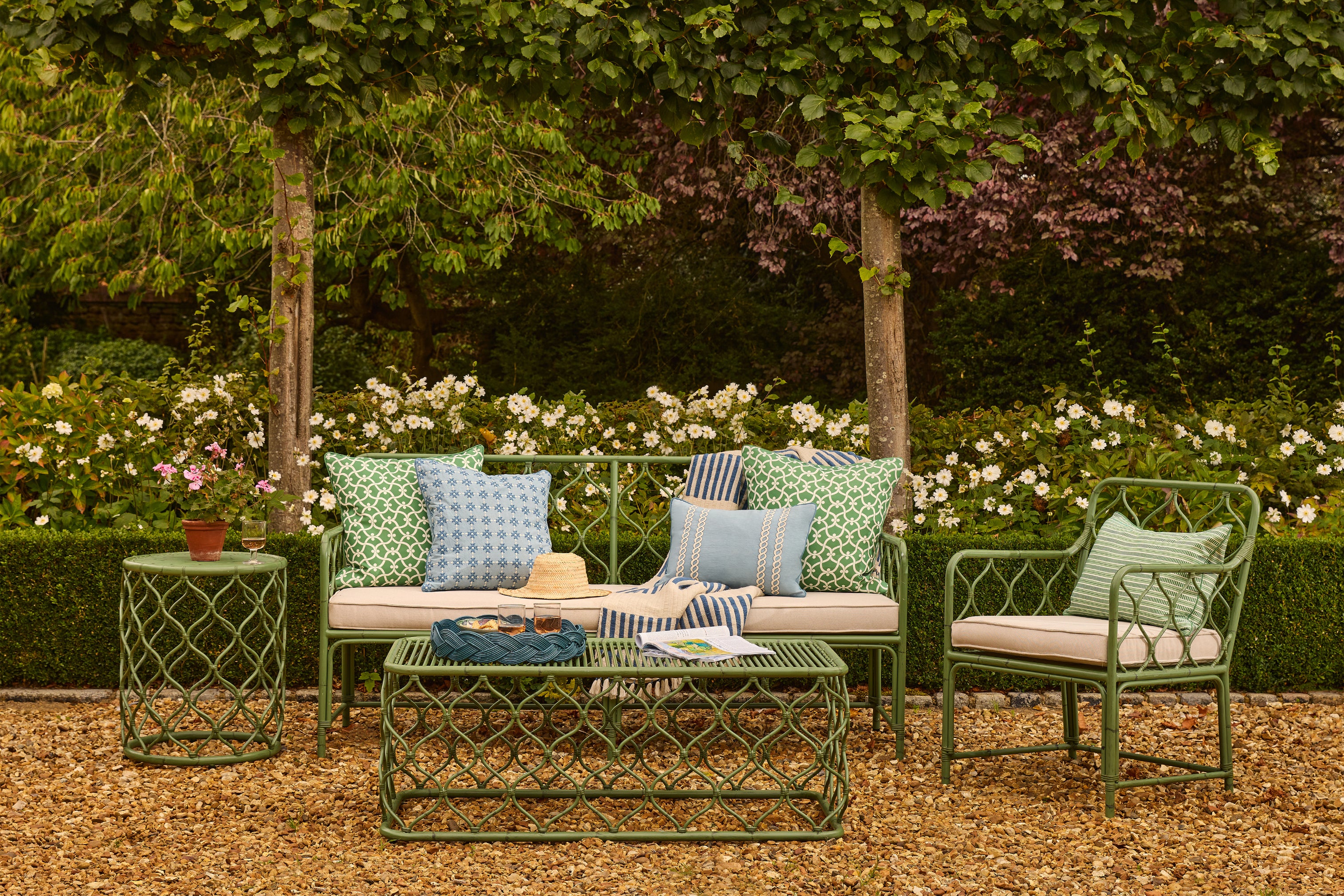 Outdoor garden set with green furniture, cushions, and a coffee table in a garden setting.