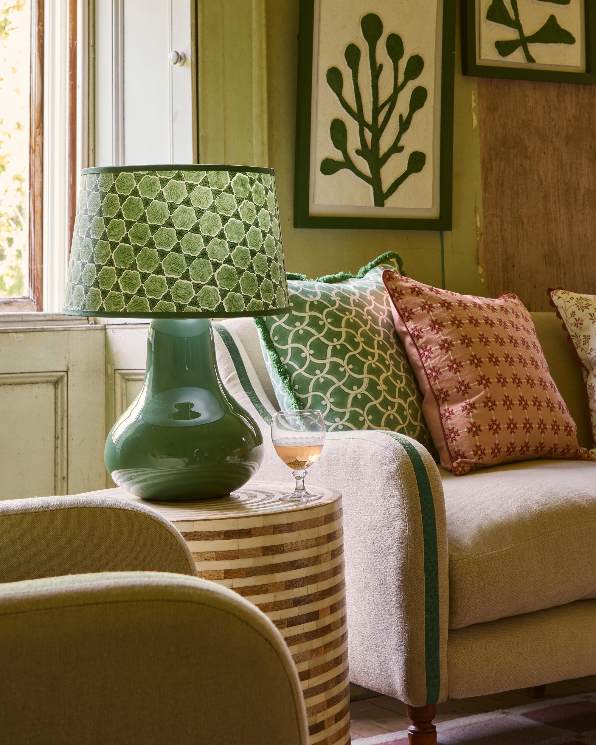 Living room with a green lamp, patterned cushions, and a glass of wine on a wooden side table.