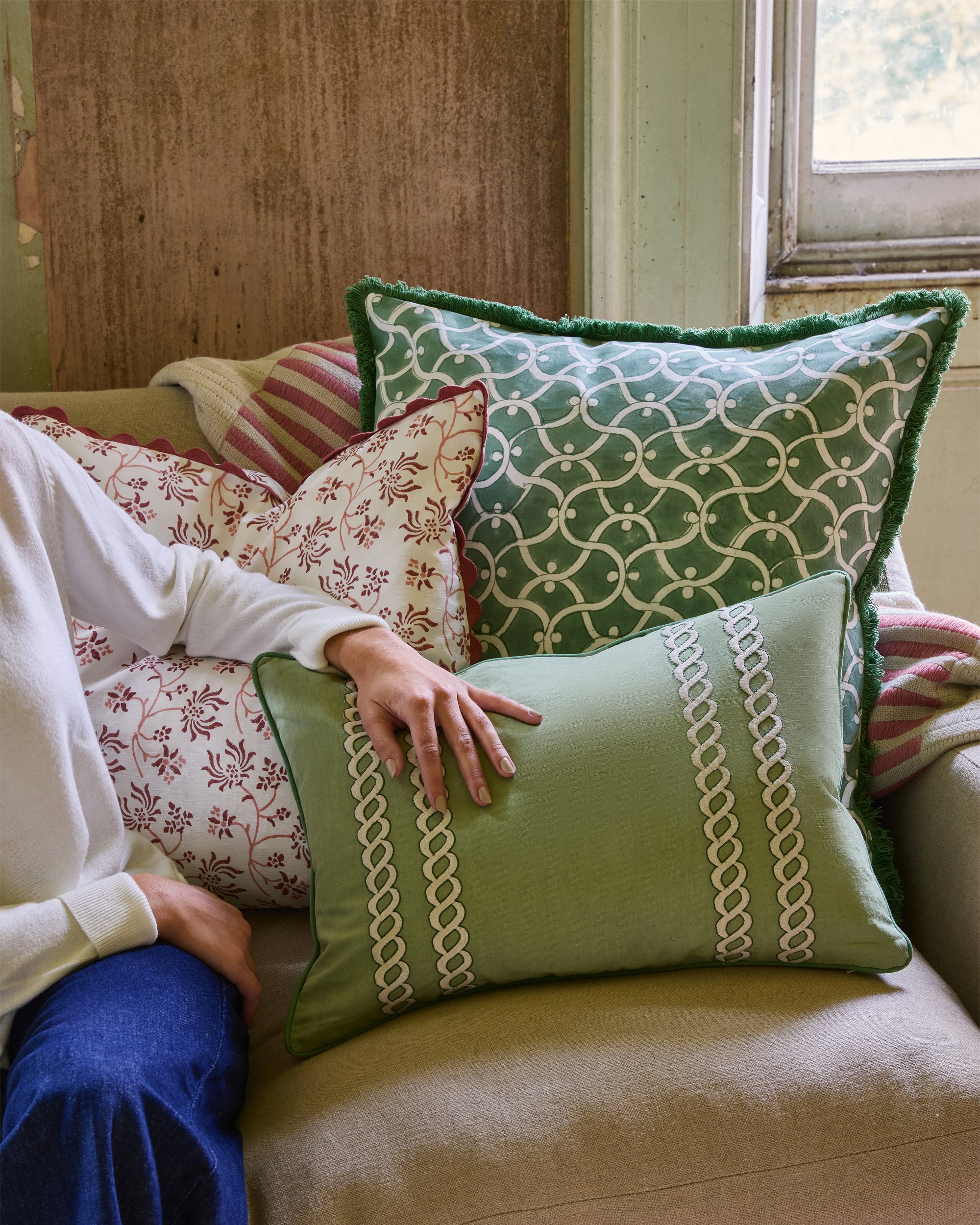 Person sitting on a couch with patterned cushions, including a green cushion with chain design.