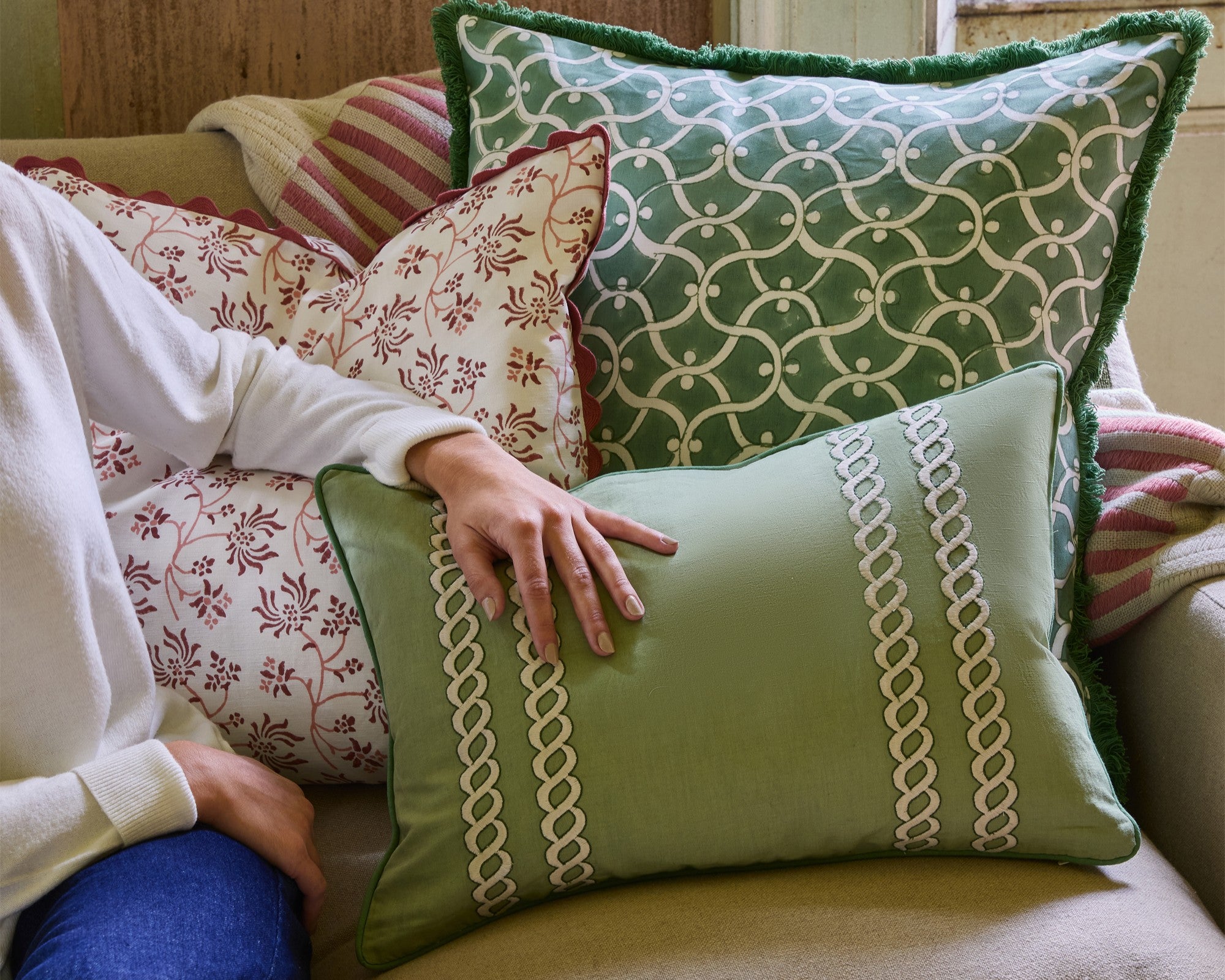 Person arranging decorative pillows on a couch with a focus on patterned cushions.