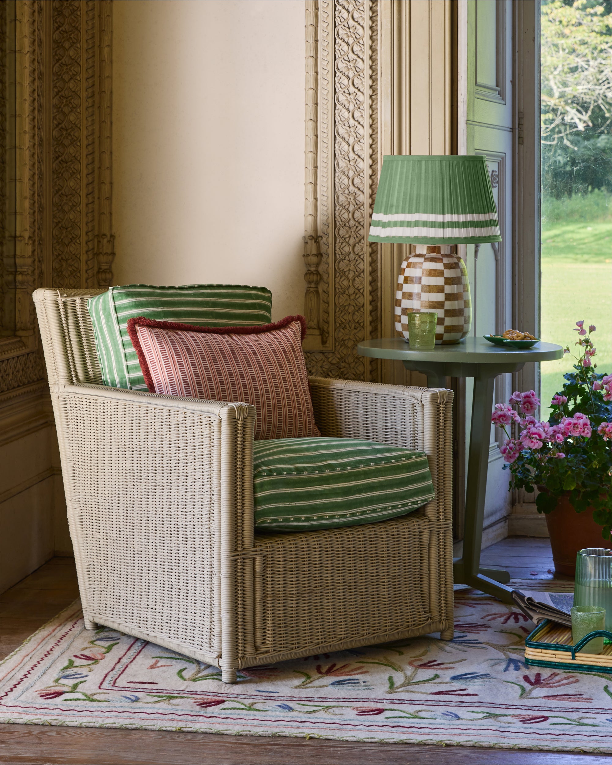Wicker armchair with striped cushions in a room with a lamp and flowers.
