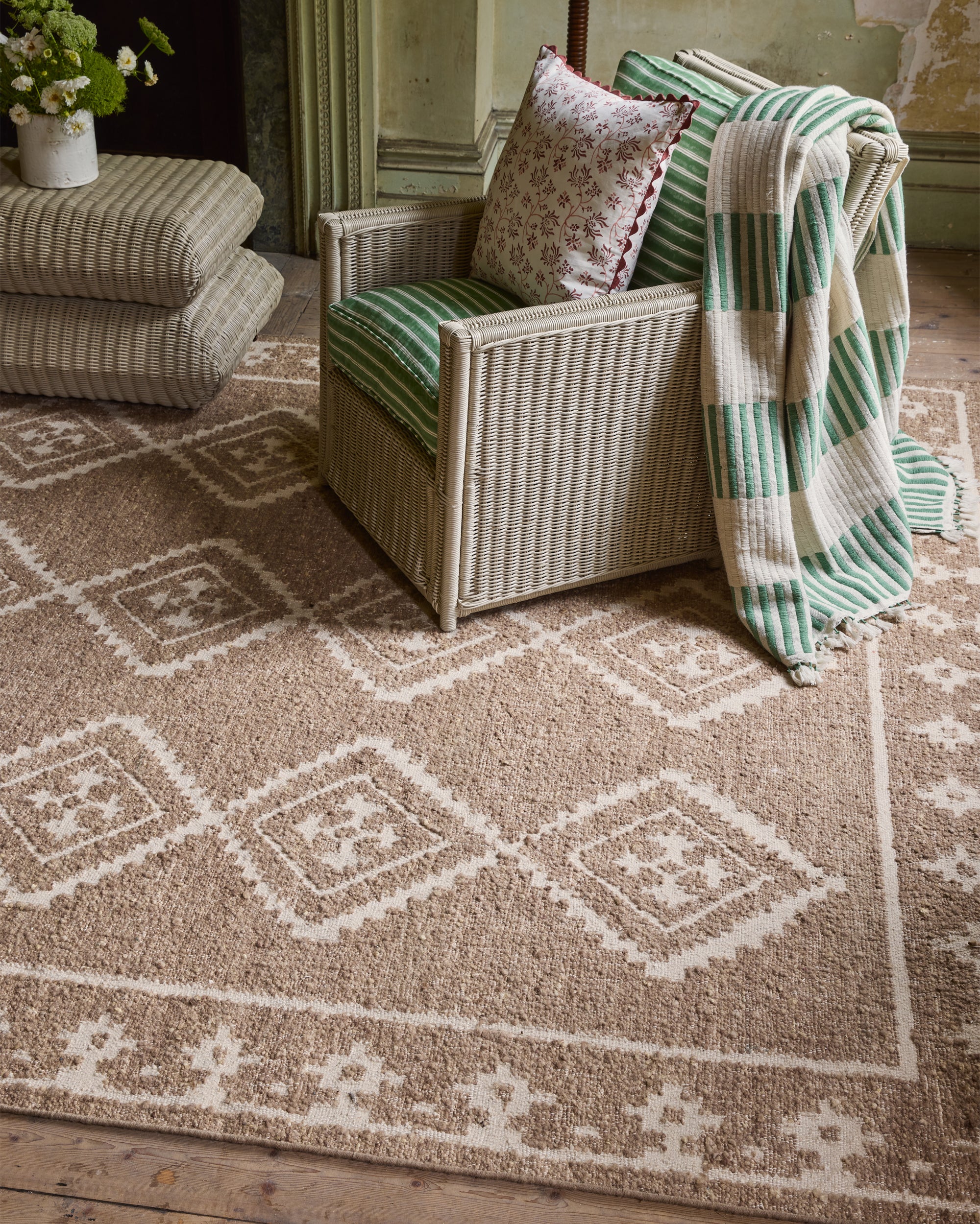 Wicker chair with cushions and a blanket on a patterned rug in a room.