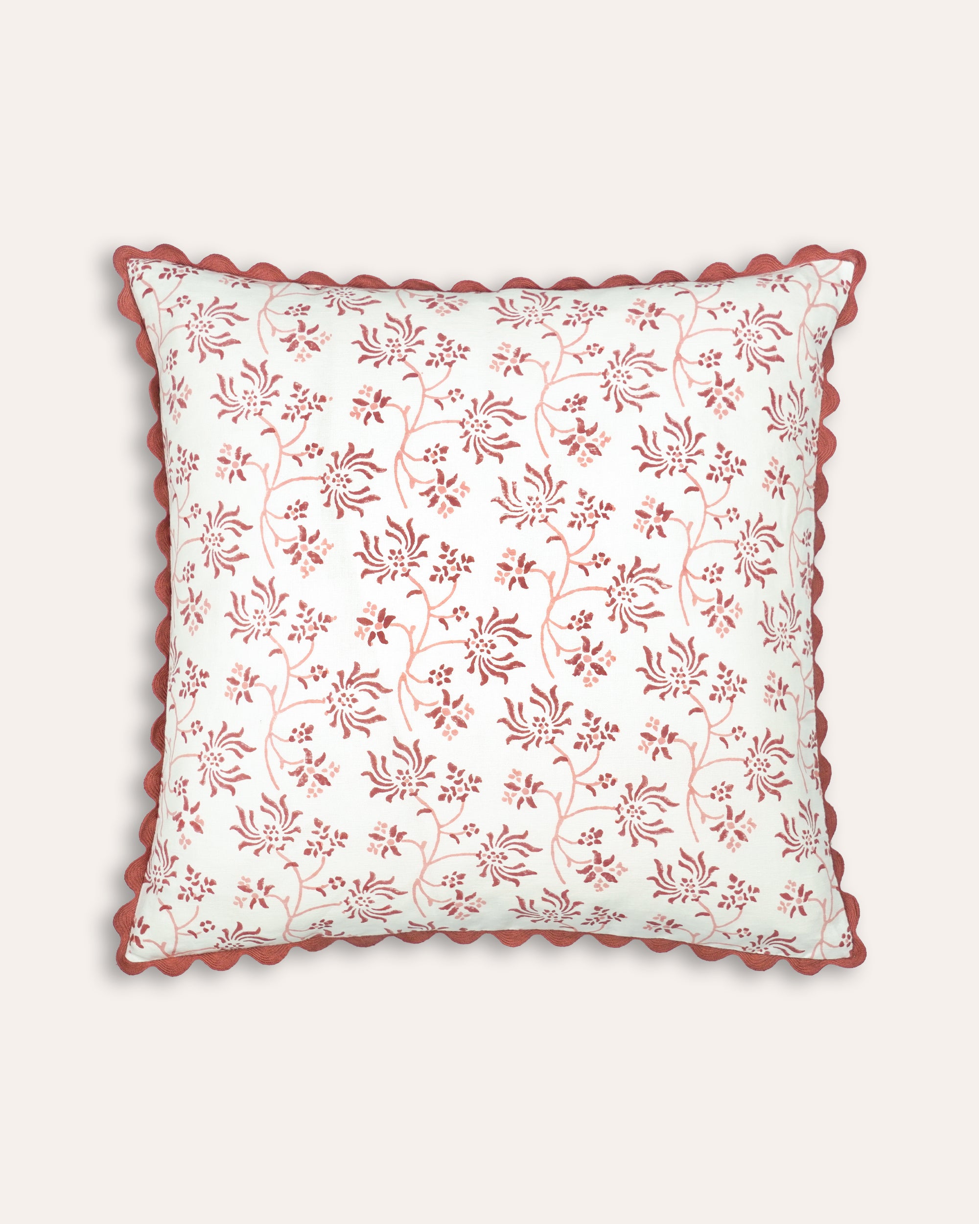 Decorative square block print cushion with floral pattern and red scalloped edge on a white background