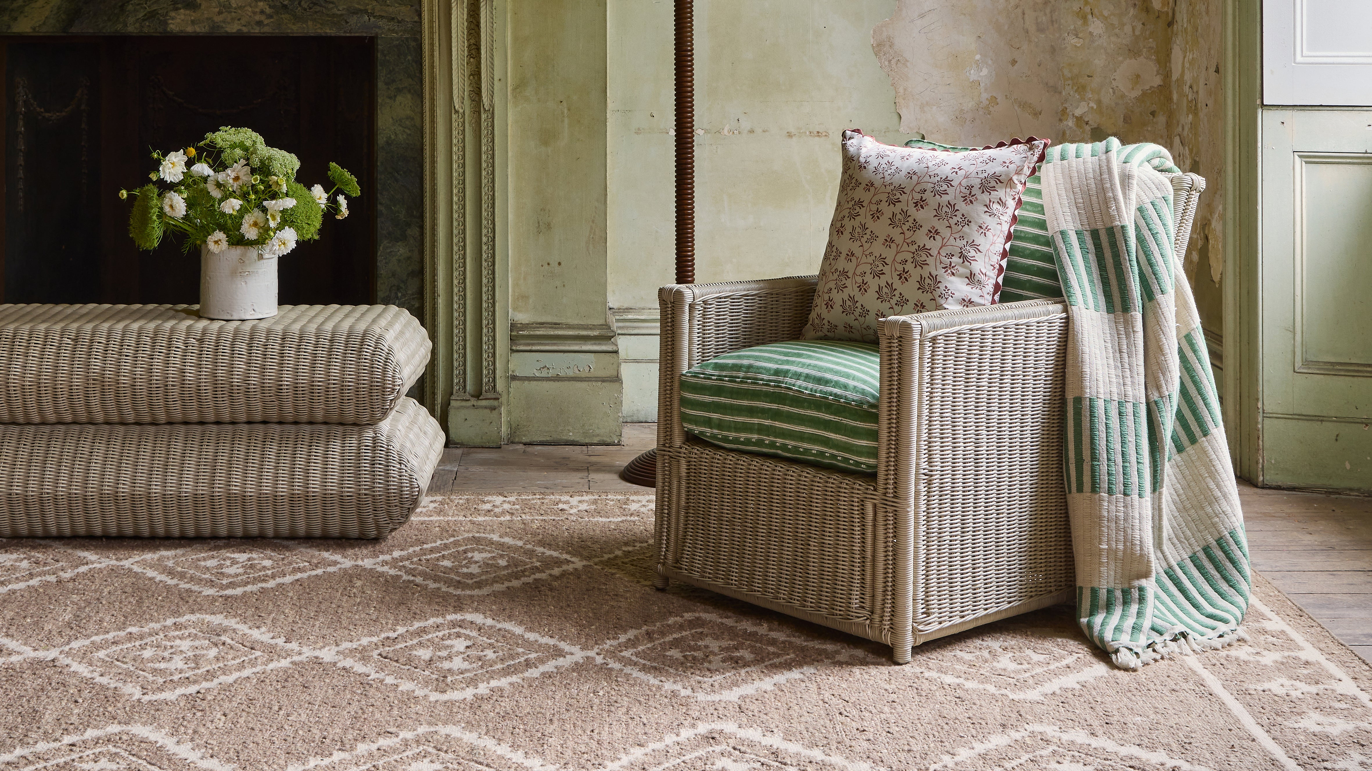Living room with rattan armchair, rattan ottoman, and floral arrangement.