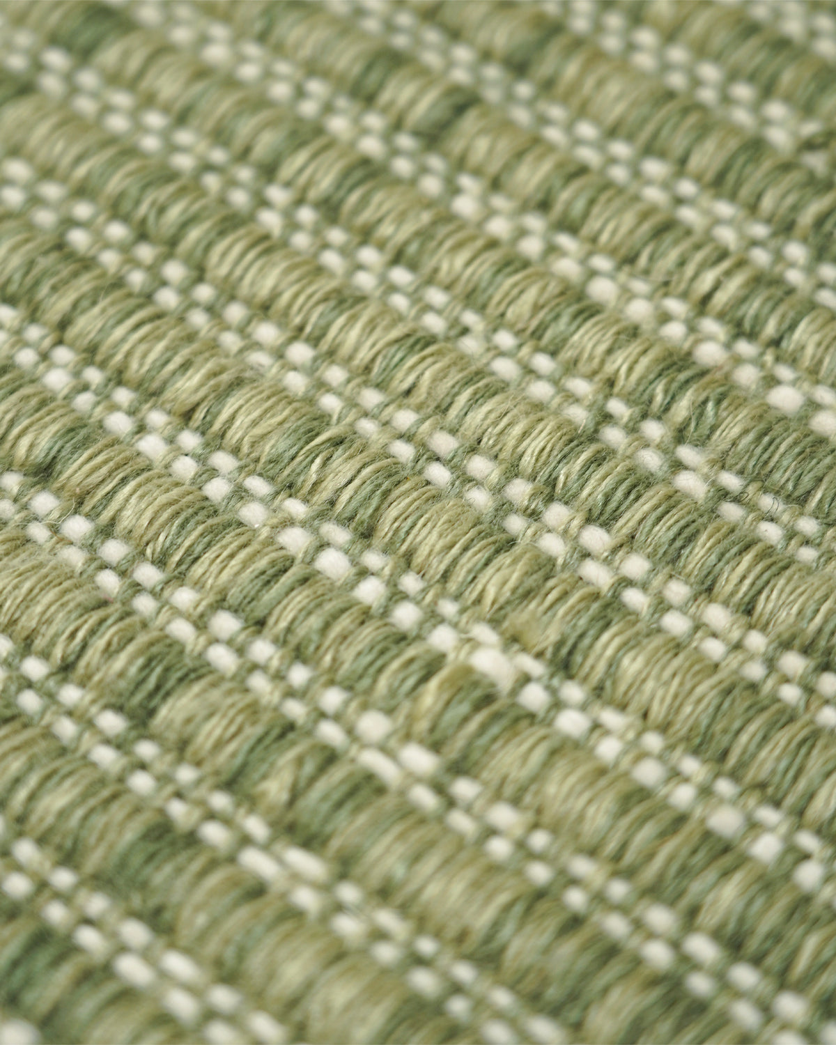 Close-up of a woven rug with a textured pattern of olive green and cream threads.