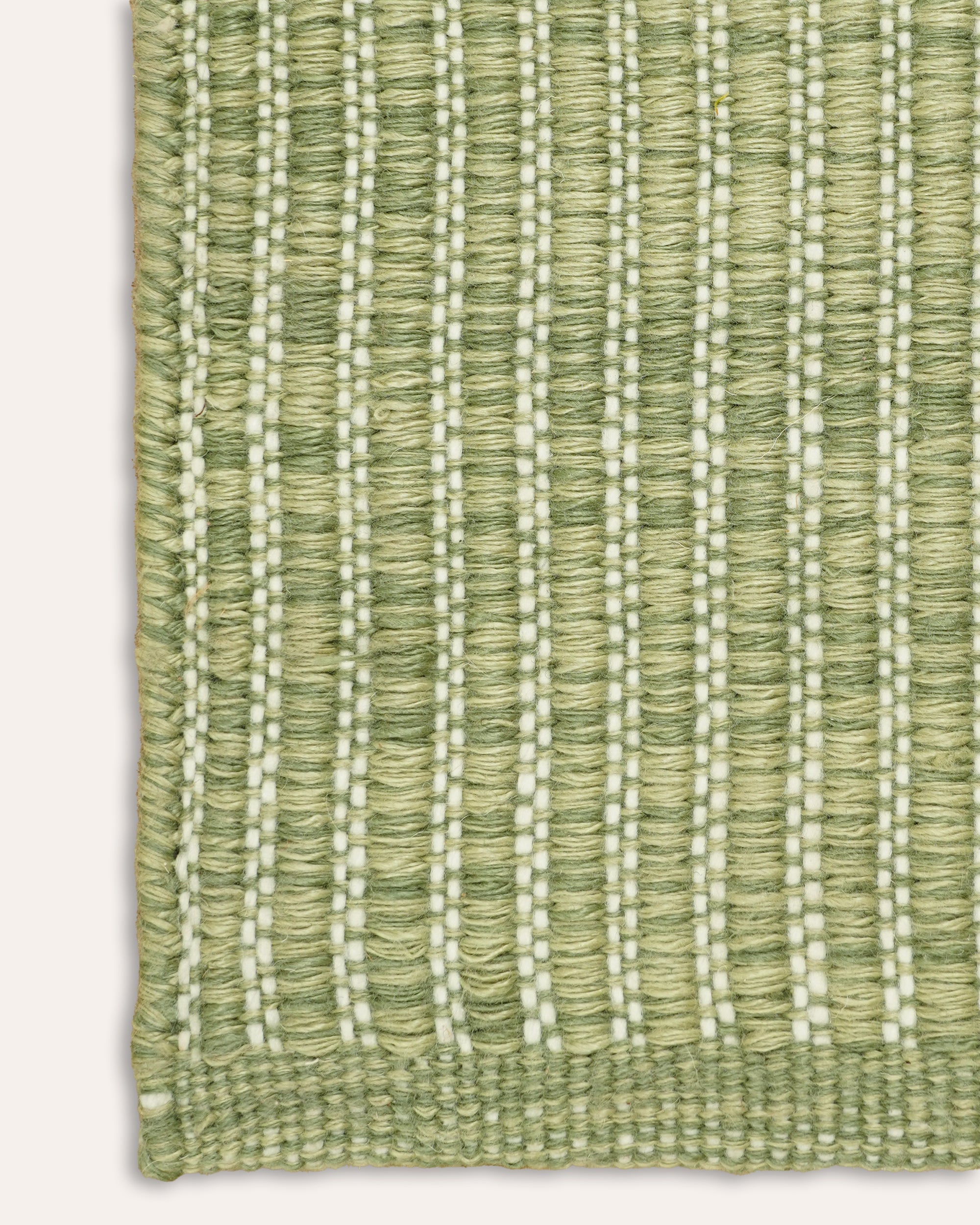 A close-up of a woven rug corner in light sage green with vertical ribbed texture and thin off-white dotted lines running through it, shown against a plain light background.