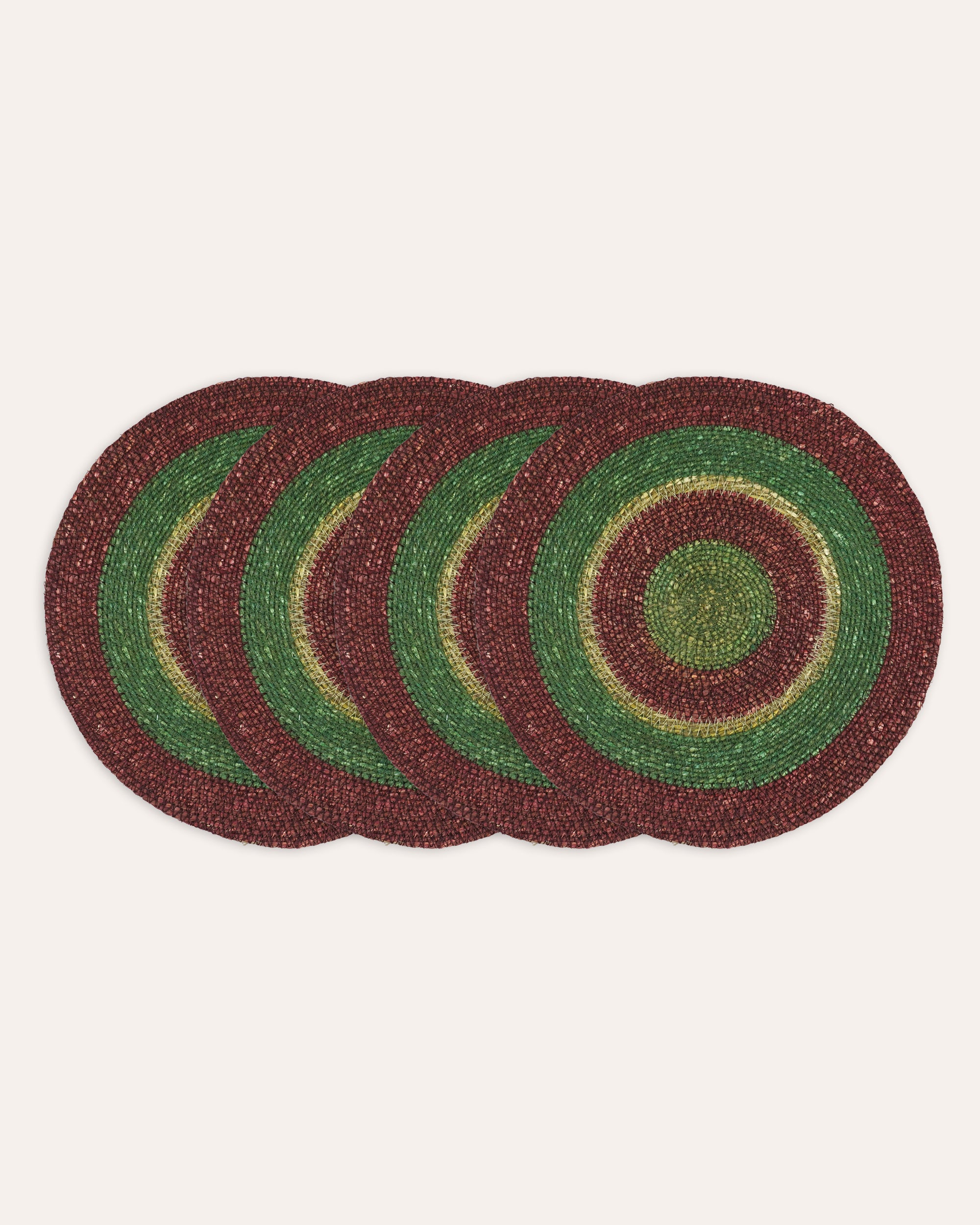 Set of four round woven placemats with green and red pattern on a white background