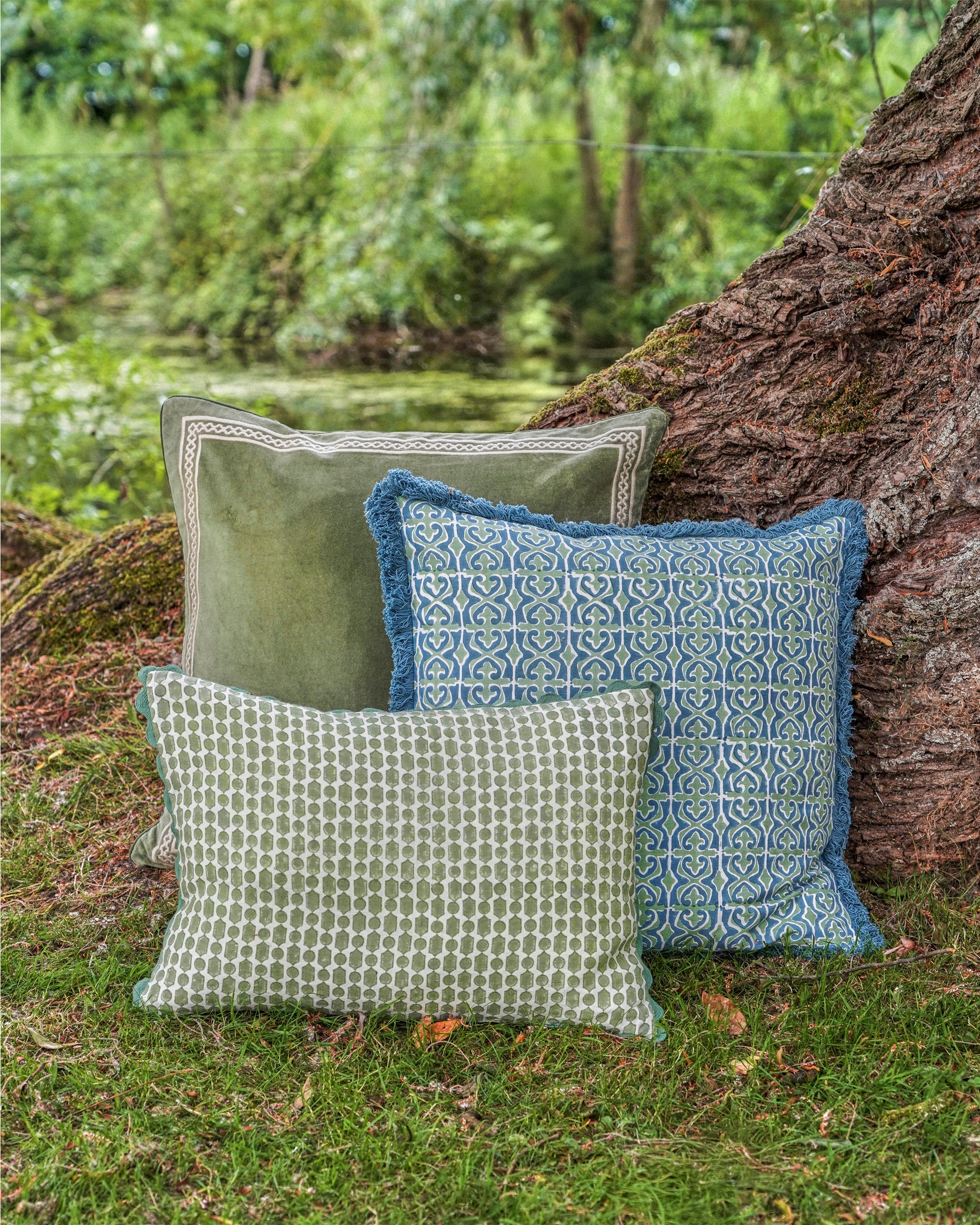 Three patterned pillows on a grassy area with a tree trunk in the background