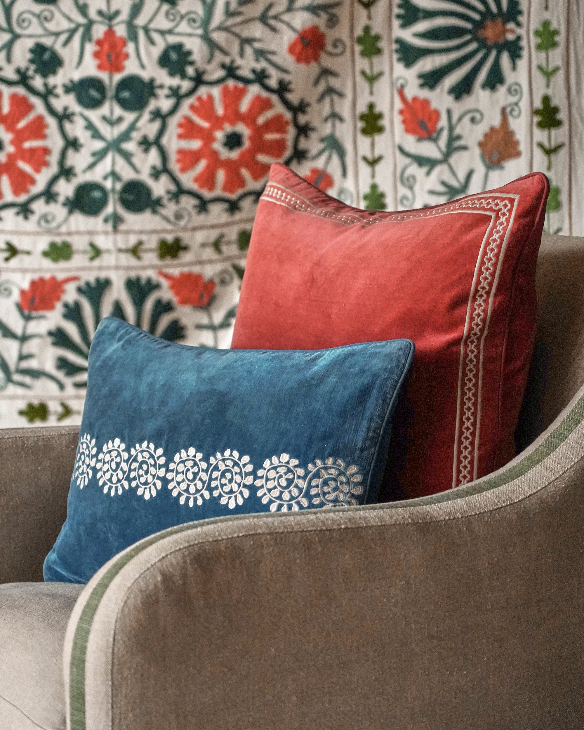 Two decorative pillows, one blue with white patterns and one red, on a sofa with a patterned wall in the background.