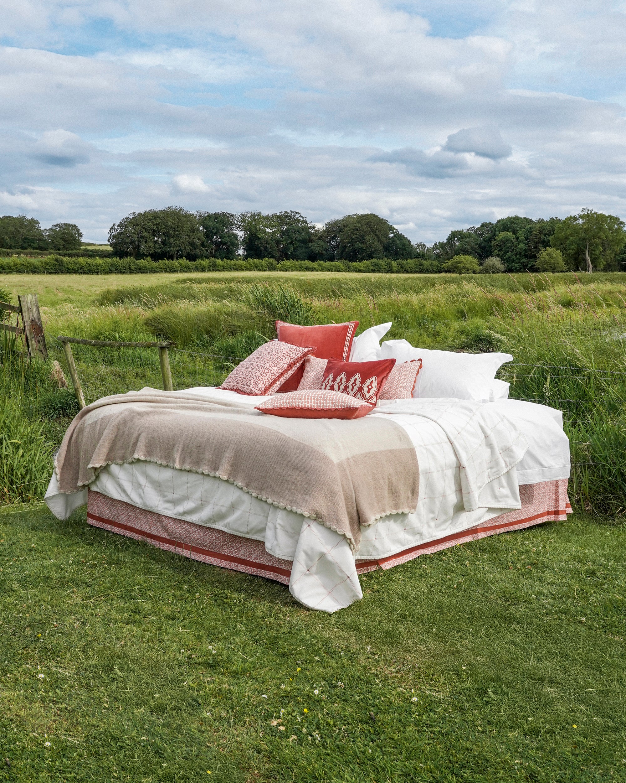 Bed with red and white bedding in a grassy field with trees in the background