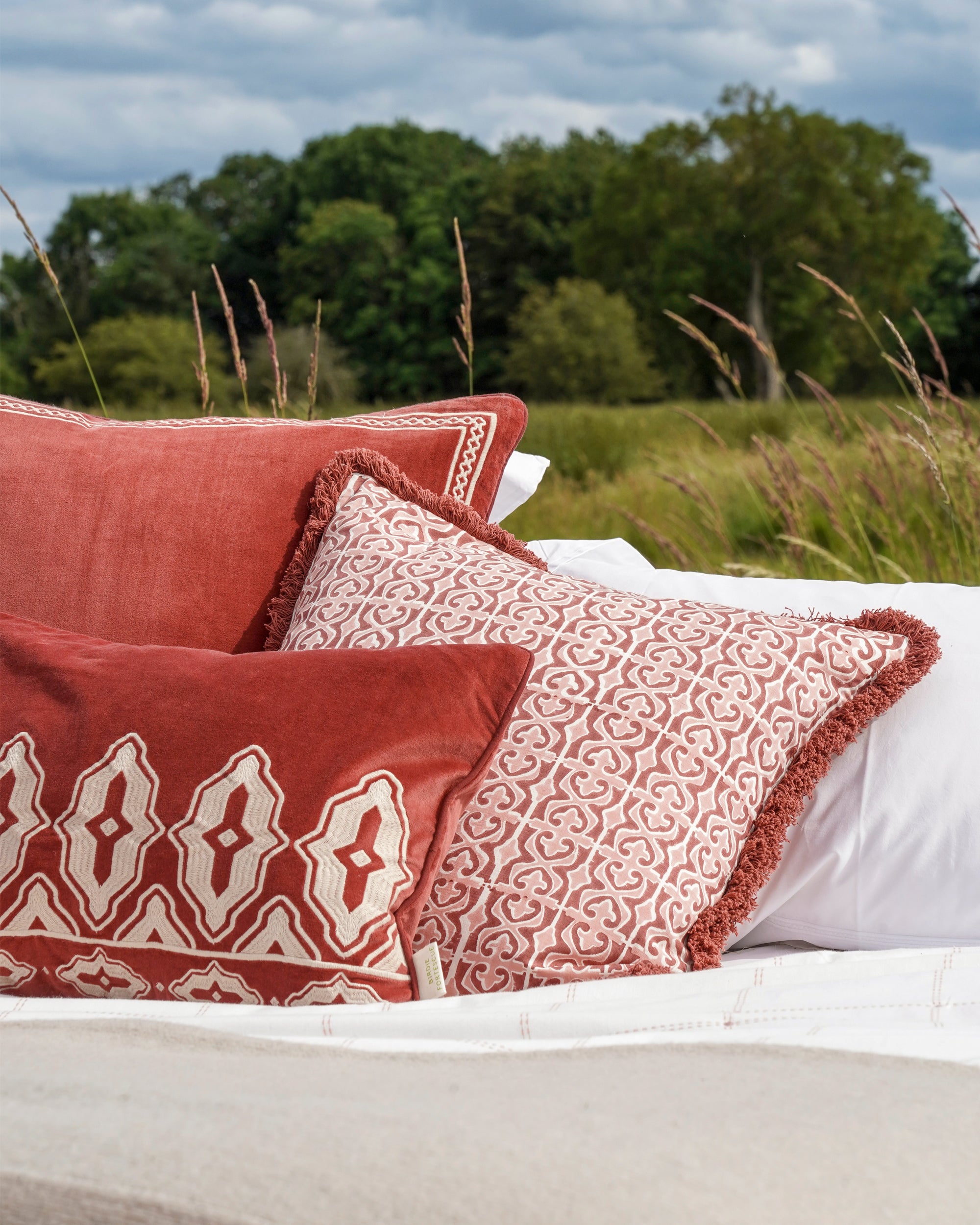Decorative pillows with intricate patterns on a bed outdoors with grass and trees in the background