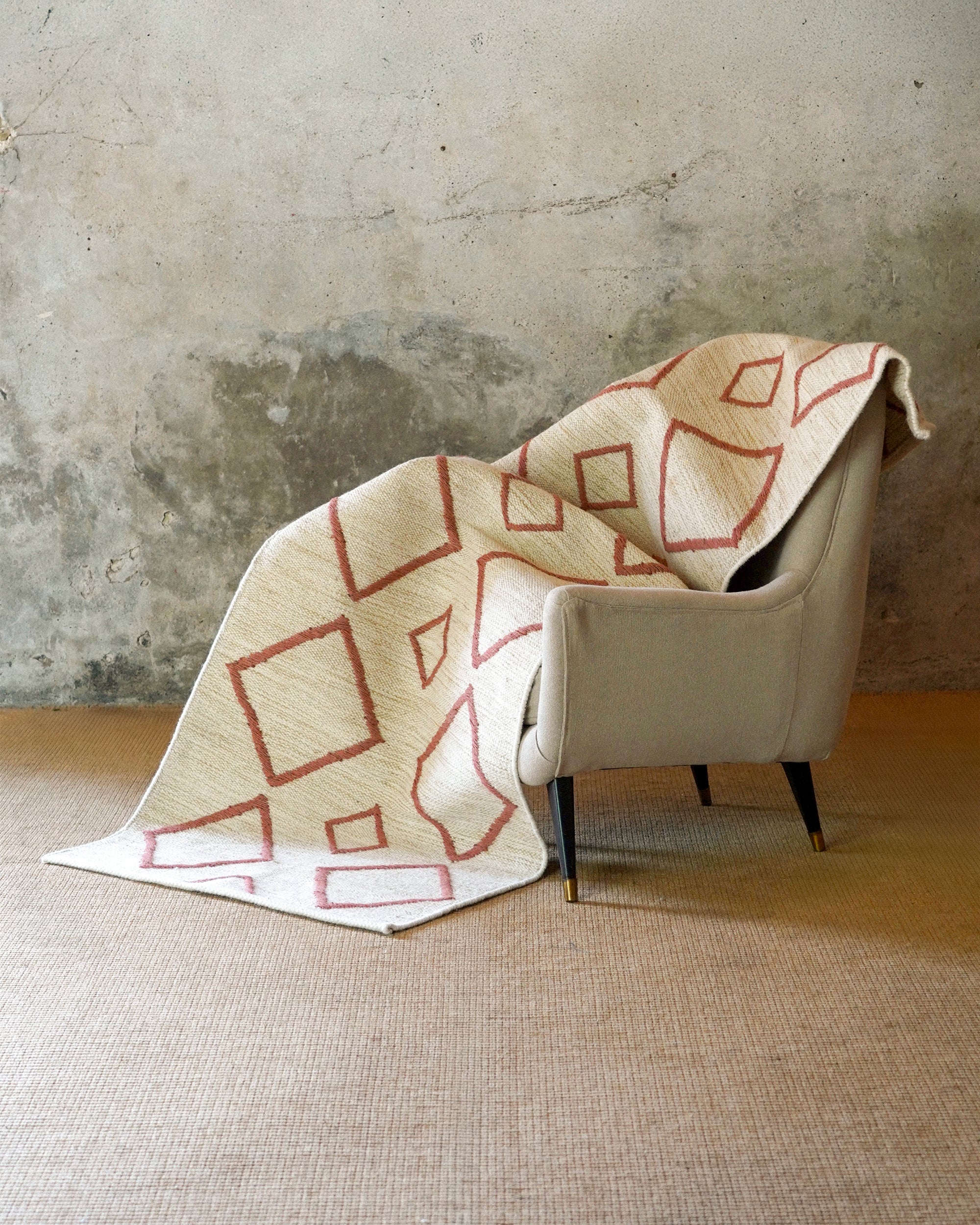 Beige armchair with a patterned beige blanket draped over it against a textured wall.