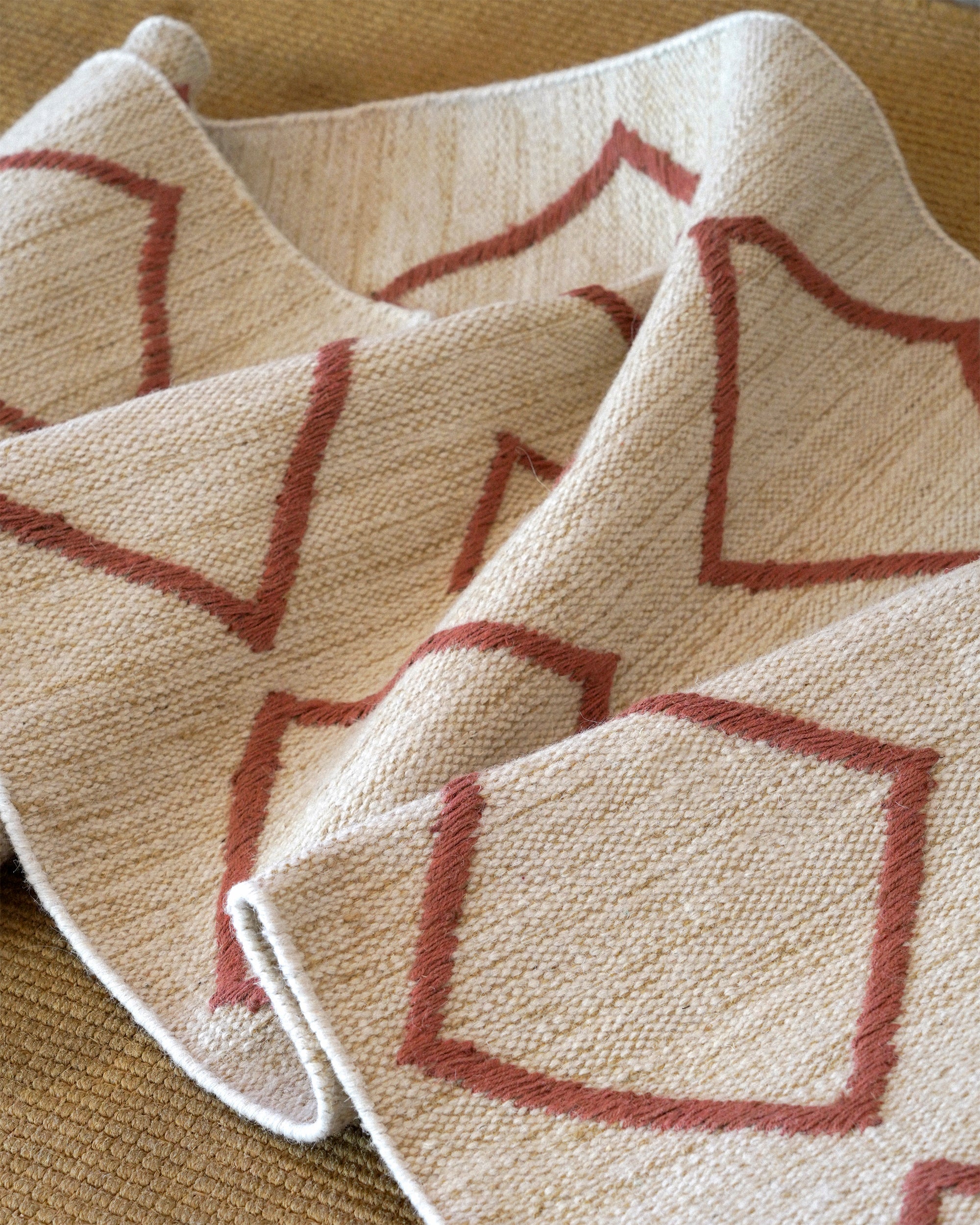 Close-up of a textured fabric with red geometric patterns on a beige background