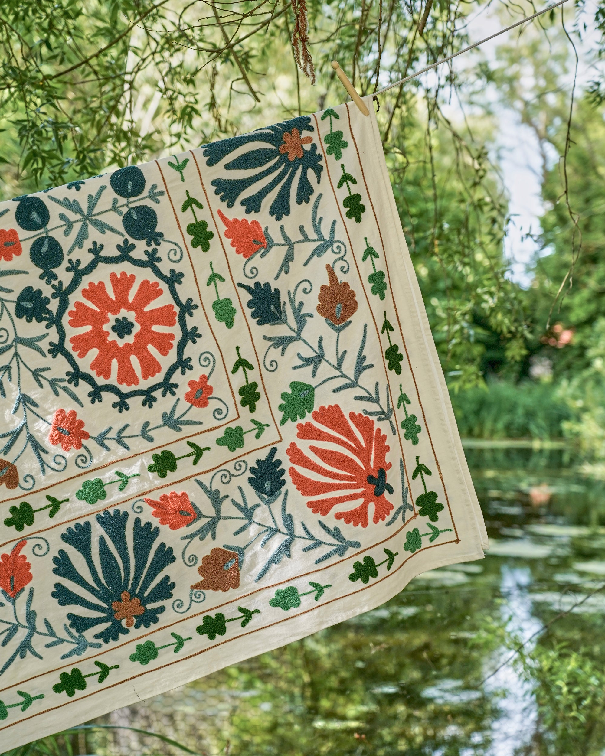 Decorative fabric with floral patterns hanging outdoors near a body of water.