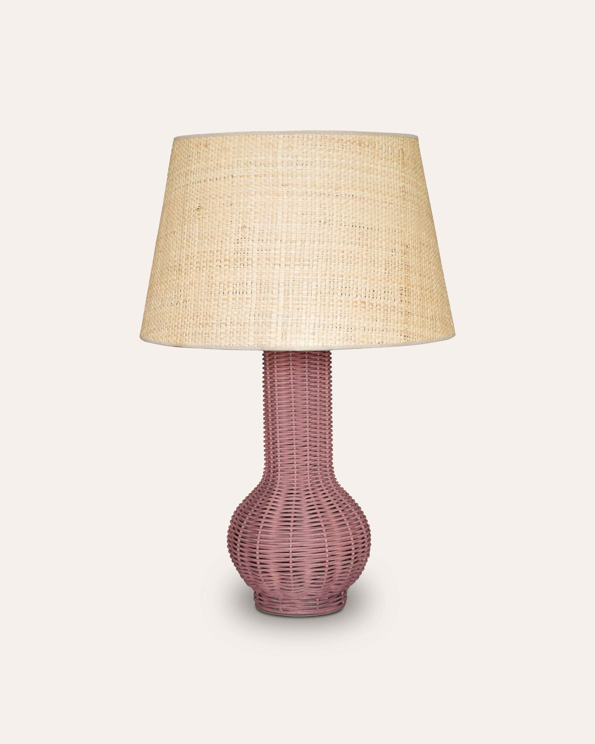 Table lamp with pink woven base and beige lampshade on a white background