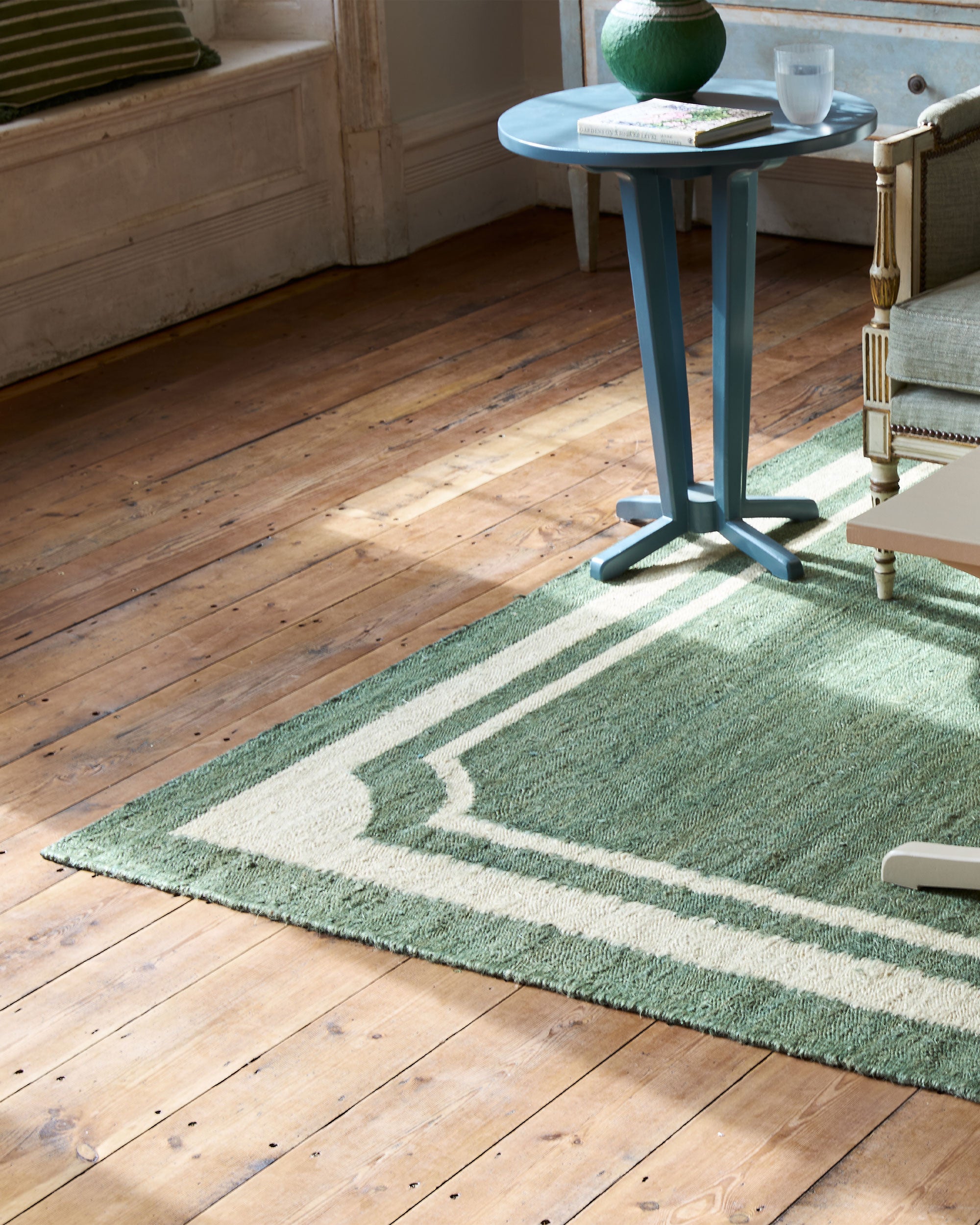 Green Villa rug on a wooden floor with a small round table and chair in the background.